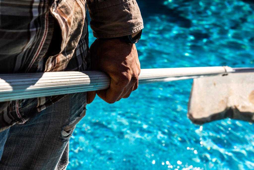 Maintenance man using a pool net leaf skimmer rake in summer to leave ready for bathing his pool.